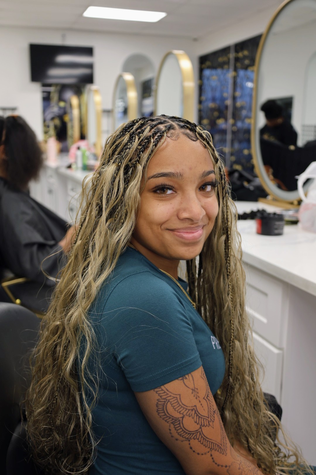 Blonde miracle knot braids seen from the side in the salon chair, the parting grid clear at the crown