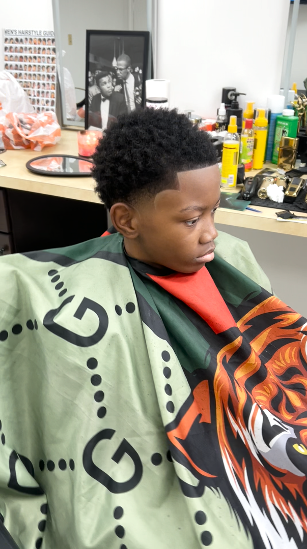 A young client with a rounded afro, taper fade and clean line-up in the barber chair