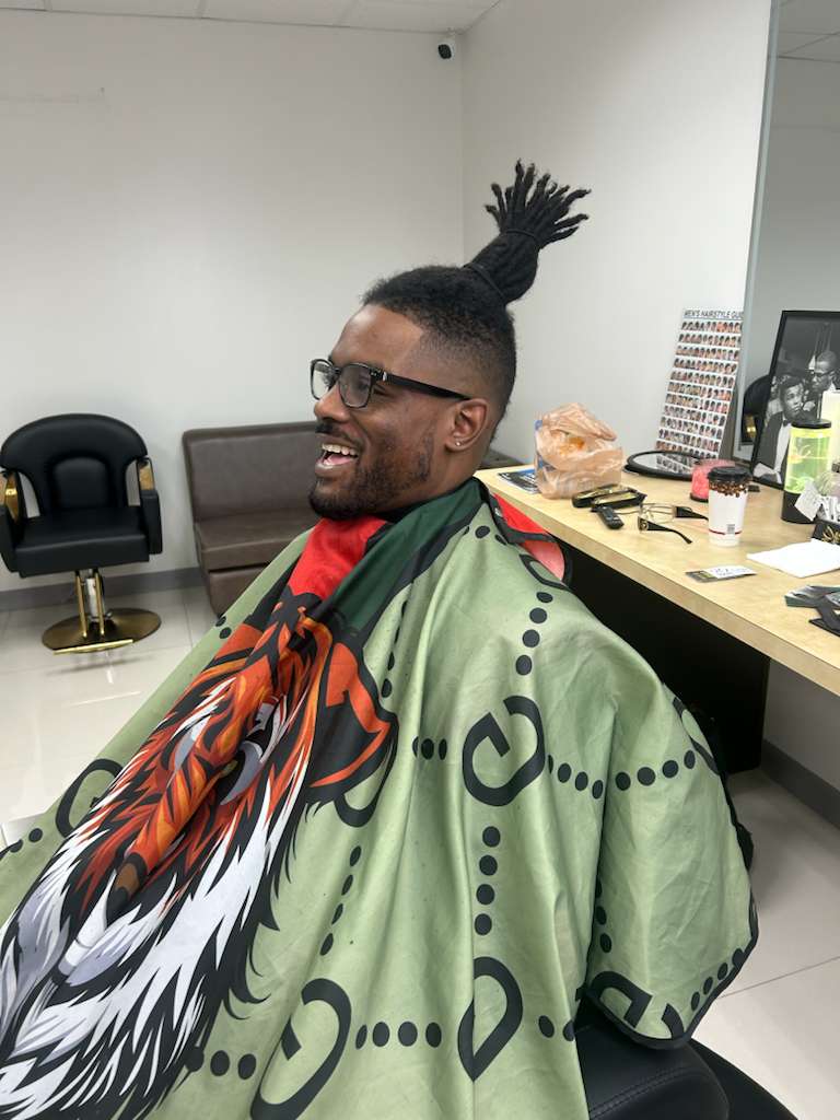 A client laughing in the barber chair after a high fade cut around a loc top knot