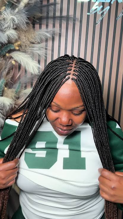 Long black box braids worn down past the chest, straight parts running back from the forehead